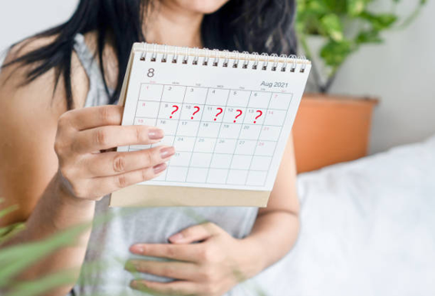 Woman holding a desk calendar with several days marked with red question marks, signaling an unclear schedule.