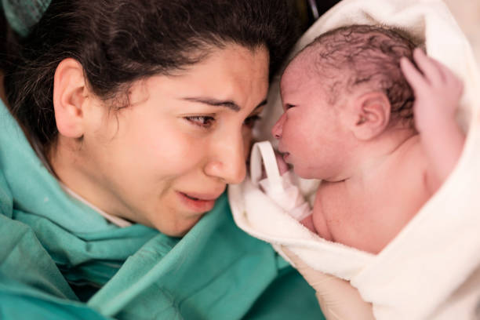 Mother and newborn share a tender, nose-to-nose moment wrapped in blankets just after birth (skin-to-skin bonding).